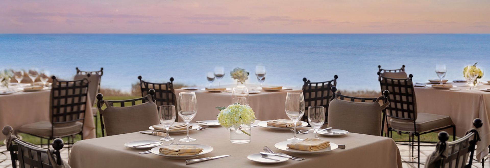 A Set Dining Table With Glasses And Plates On It By The Water